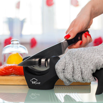 Manual 3-stage professional knife sharpener with diamond, tungsten steel, and ceramic slots being used to sharpen a kitchen chef knife.