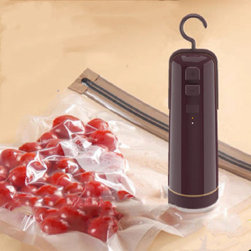 Compact handheld electric vacuum sealer being used on a reusable textured storage bag for sous vide cooking preparation.