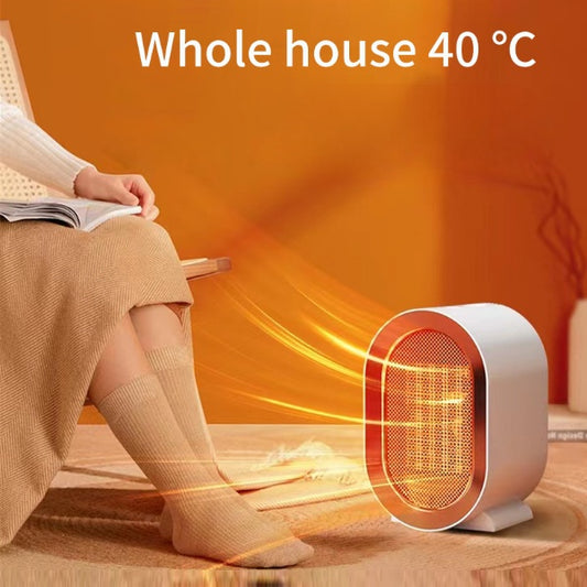 Compact black portable electric space heater on an office desktop, showing the front grill with warm PTC ceramic heating element active.