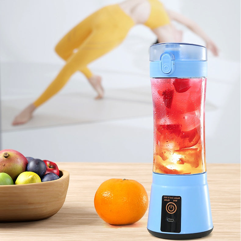 Blue portable blender with red and orange juice on a wooden table with fruits in the background.